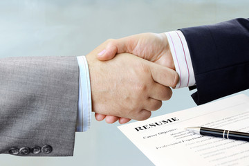 Closeup of handshake with office table and resume background 