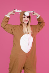 happy young woman posing in deer costume in studio on pink background 