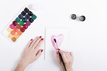 Female hands with red nail polish painted watercolor heart in a