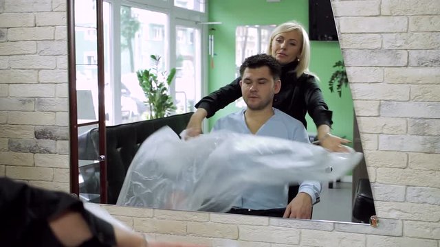 A man at hairdresser's. Female barber preparing a young man to having the hair cut. HD