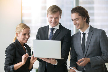 Group of three businesspeople discussing new project at meeting in office room, using laptop. Middle aged businessman leader showing work results to his team using laptop. Business success concept