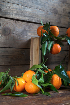 Tangerines with leaves on wooden box over old wooden table. Dark rustic style.