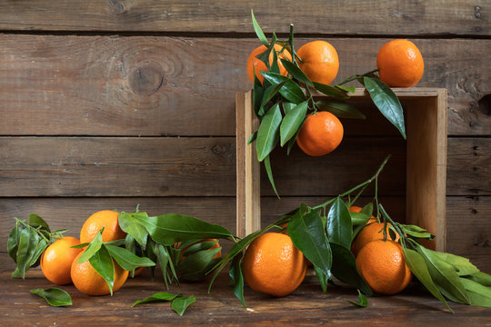 Tangerines with leaves on wooden box over old wooden table. Dark rustic style.