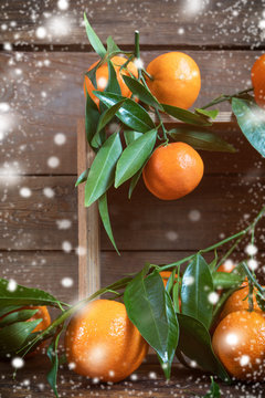Tangerines with leaves on wooden box over old wooden table. Dark rustic style with falling snow and retro filter effect.