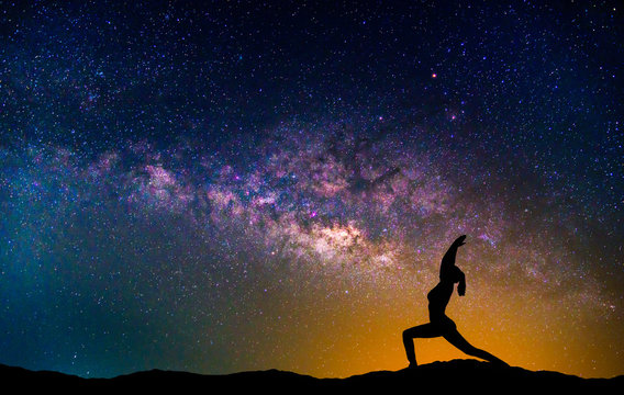 Landscape with Milky way galaxy. Night sky with stars and silhouette woman practicing yoga on the mountain.