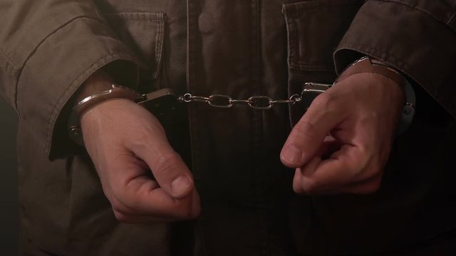 Arrested criminal, nervous cuffed male hands in dark prison room, close up