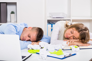 Exhausted businessman and businesswoman are sleeping at work.
