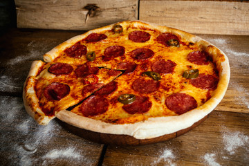 Whole pizza with sausages and pepper on wood table with ingredients
