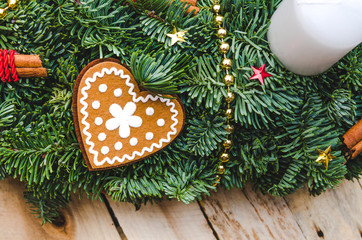 Advent Christmas wreath made natural pine with Heart shaped gingerbread cookie, red decorations, cinnamon stick, gold beads, star confetti on rustic wooden background.