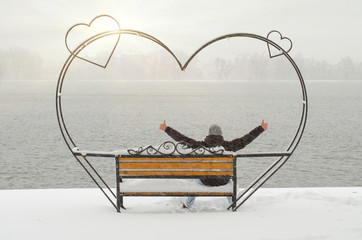 Unrecognizable man sitting on the beautiful wrought iron bench of love in the park with pond and enjoying beautiful winter day in solitude.