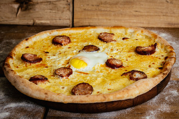 Pizza with sausages and egg on wood background