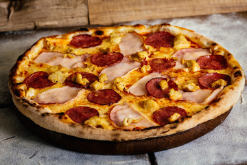 Pizza with ham, sausages and chicken on wood background