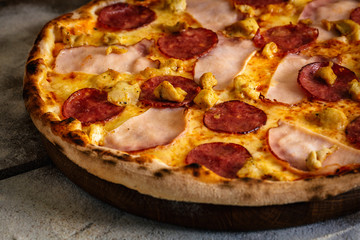 Pizza with ham, sausages and chicken on wood background