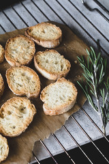 Crostini with rosemary olive oil on parchment paper on cooling rack. Selective focus, vertical composition, desaturated colors.