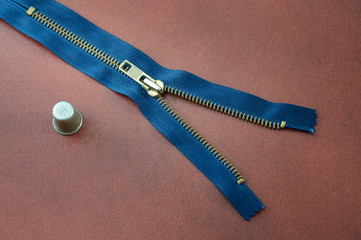 blue metal zipper with a thimble on leather background