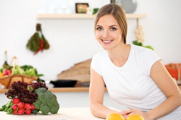 Young cheerful smiling woman is ready for cooking in a kitchen. Housewife sitting at the table and looking at the camera