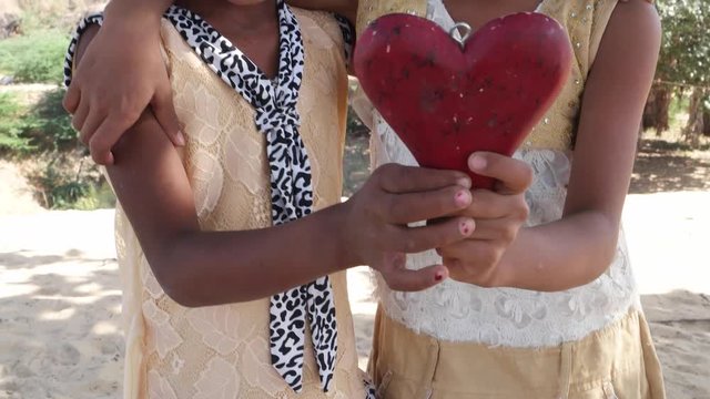 Two cute girl friends with a wooden heart shaped block in their hands 