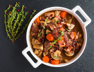 Beef Bourguignon in a casserole on black stone. Stewed with bacon, garlic, carrots, onions, mushrooms,  red wine, fresh thyme and spices. Top view. - 129695403