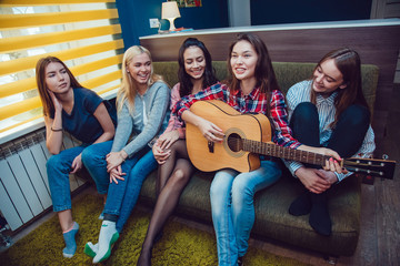 Obraz premium Beautiful girls sitting on couch, have fun and play the guitar in Hostel.