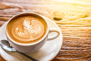 cup of the latte art coffee with spoon and plate on the brown bark beautiful texture background with warm light