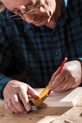 Close up of senior carpenter hands taking measurement on a wooden plank in workshop