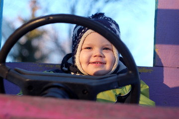 Мальчик трех лет улыбается за рулем игрушечного автомобиля 