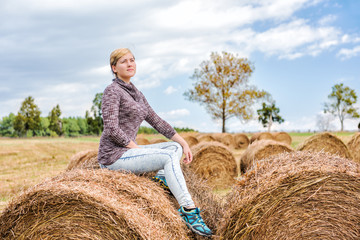 Naklejka na ściany i meble Young woman sitting on hay roll bale