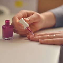 Woman paints her nails with pink nail polish