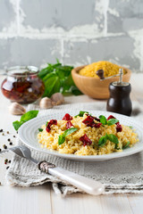 Bulgur with dried tomatoes and basil on a light wooden background. Vegetarian dish. Selective focus.