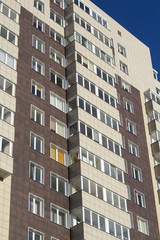 Detail of a modern high-rise multilevel building with right angles, with dark blue glass windows with metal frames and walls overlaid with natural beige travertine, with the prospect of a blue sky