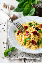Bulgur with dried tomatoes and basil on a light wooden background. Vegetarian dish. Selective focus.