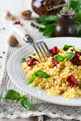 Bulgur with dried tomatoes and basil on a light wooden background. Vegetarian dish. Selective focus.
