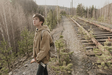 young boy walking on railroad tracks. He is holding the gun. wandering boy. man in a protective...