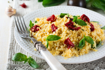 Bulgur with dried tomatoes and basil on a light wooden background. Vegetarian dish. Selective focus.