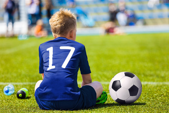 Young Soccer Football Player. Little Boy Sitting on Soccer Pitch. Youth Football Player in Blue Soccer Jersey