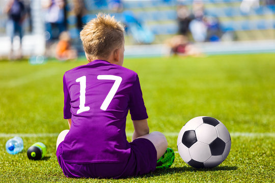 Young Soccer Football Player. Little Boy Sitting on Soccer Pitch. Youth Football Player in Purple Soccer Jersey