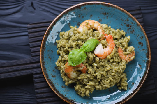 Risotto with spinach and tiger shrimps on a black wooden surface