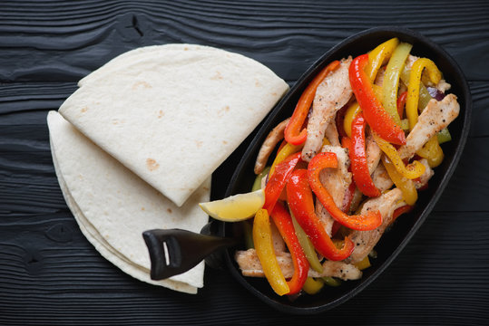 Chicken fajitas in a cast-iron pan with tortillas, flat-lay view