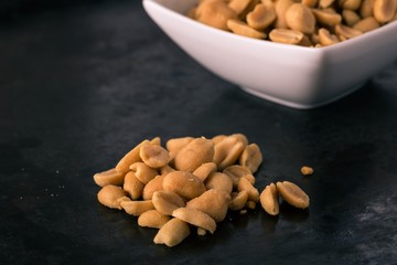 Dark tray with salted peanuts on heap and in bowl