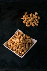 Dark tray with salted peanuts on heap and in white bowl