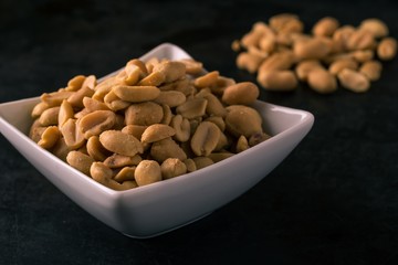 Peanuts in white bowl on dark tray