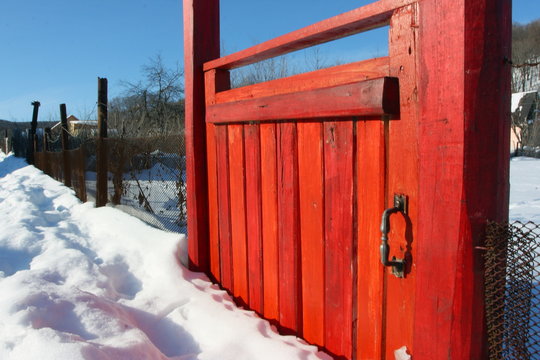Red wooden gate mostly covered with snow in the village against a blue sky