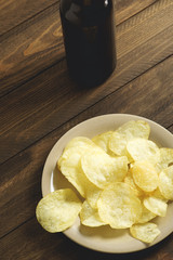 Plate with chips and beer bottle standing on dark brown wooden table. Vertical studio shot