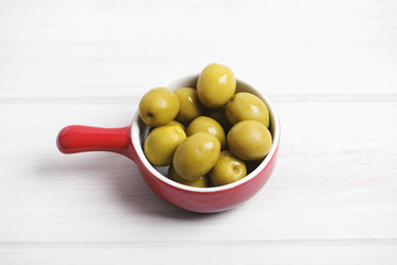 Small red dish filled with olives standing on pale gray colored wooden table. Horizontal studio shot