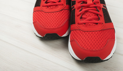 Red sneakers standing on pale gray wooden floor. Horizontal studio