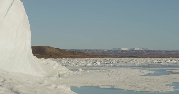 Pan from Ice mound to Inuit on snow machine with komatik