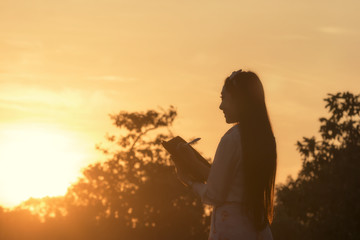 Young woman reading a book at meadow in summer sunset light.