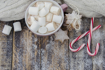 Cup of coffee with marshmallow, cookies and candy canes on dark wooden background