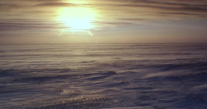 Sun near horizon through clouds in blizzard over tundra