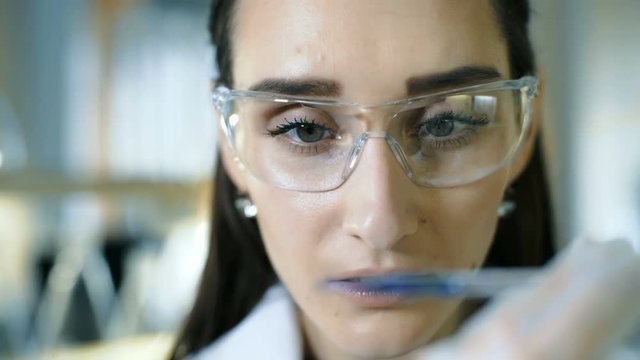 Young female scientist holding test tube with liquid sample making research in clinical laboratory
